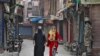 FILE - A Kashmir girl rides her bike past Indian security force personnel standing guard in front of closed shops on a street in Srinagar, Oct. 30, 2019.