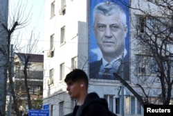 Muškarac hoda pored transparenta sa bivšim predsednikom Kosova Hašimom Tačijem, u Prištini, Kosovo, 30. mart 2023.