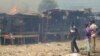 Men stand and watch as a fire rages in the background during clashes between rival gangs in Marche Madina, in Conakry Mar. 1, 2013