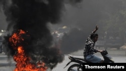 A man flashes the three-finger salute as he passes burning tires during a protest against the military coup, in Mandalay, Myanmar, April 1, 2021.