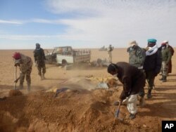 FILE - Volunteers and officials dig graves to inter the bodies of migrants who died of thirst after their the truck they were traveling in, seen rear, broke down while attempting to cross the Sahara Desert north of Arlit, Niger, Oct. 30, 2013.