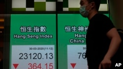 A man wearing a face mask walks past a bank's electronic board showing the Hong Kong share index at Hong Kong Stock Exchange Monday, March 30, 2020. Asian shares started the week with further losses as countries reported surging numbers of…