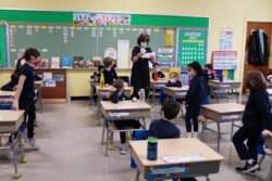 FILE - A teacher calls names for schoolchildren to collect a swab and test themselves for COVID-19 to prevent the spread of the coronavirus disease (COVID-19) in the classroom at South Boston Catholic Academy in Boston, Massachusetts, Jan. 28, 2021.
