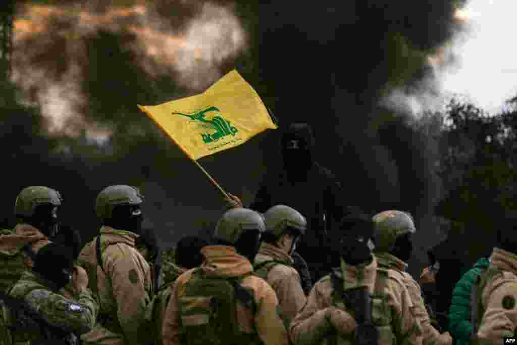 A Hezbollah supporter waves the group's flag in front of Lebanese army troops, as protesters burn tires to block the road leading to Beirut's international airport, during a demonstration against statements made by U.S. deputy special envoy for Middle East peace Morgan Ortagus after she met with the country's president, in Beirut, Lebanon.