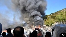 Migrants watch smoke rising from a fire inside a refugee camp on the eastern Aegean island of Samos, Greece, Nov. 11, 2020. 