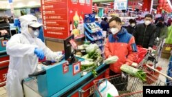 A worker in protective suit serves customers at a checkout counter of a supermarket following the outbreak of the novel coronavirus in Wuhan, Hubei province, China February 12, 2020. China Daily via REUTERS ATTENTION EDITORS - THIS IMAGE WAS…
