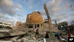 Orang-orang berdiri di luar masjid yang hancur akibat serangan udara Israel di Khan Younis, Jalur Gaza, Minggu, 8 Oktober 2023. (Foto: AP)