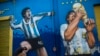 Augusto Canosa berdoa sambil menyentuh lukisan Diego Maradona di dekat stadion Boca Juniors di Buenos Aires, Argentina, 27 November 2020. (Foto: AP)