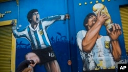 Augusto Canosa berdoa sambil menyentuh lukisan Diego Maradona di dekat stadion Boca Juniors di Buenos Aires, Argentina, 27 November 2020. (Foto: AP)