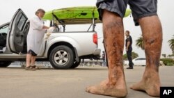 In this photo provided by the Santa Barbara County, Calif., Fire Department, Henry Duncan, left, and Bob Seiler, legs covered in oil, foreground, stand in the Goleta Beach parking lot with their oil-covered kayaks, on the truck at rear, in Goleta, California, Wednesday, July 29, 2015. 