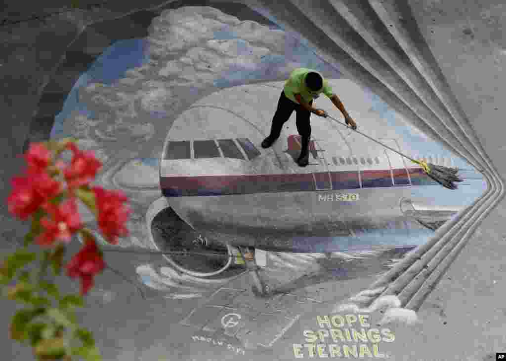Seorang pekerja membersihkan gambar mural pesawat Malaysia Airlines Flight 370 di sekolah Benigno "Ninoy" Aquino di kota Makati, Filipina.