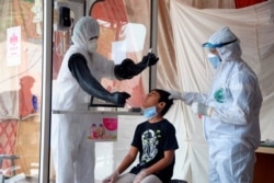 FILE - Health workers take a nasal swab sample during a testing and screening operation for the new coronavirus, in Hyderabad, Pakistan, June 26, 2020.