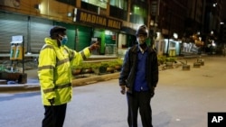 FILE - A Kenyan police officer stops a man who was heading home past the start of the daily dusk-to-dawn curfew in the Eastleigh area of Nairobi, Kenya.