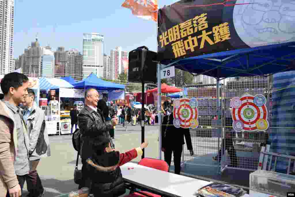 有家長帶同小朋友在香港工黨維園年宵市場的攤位,玩惡搞港府高官的飛標