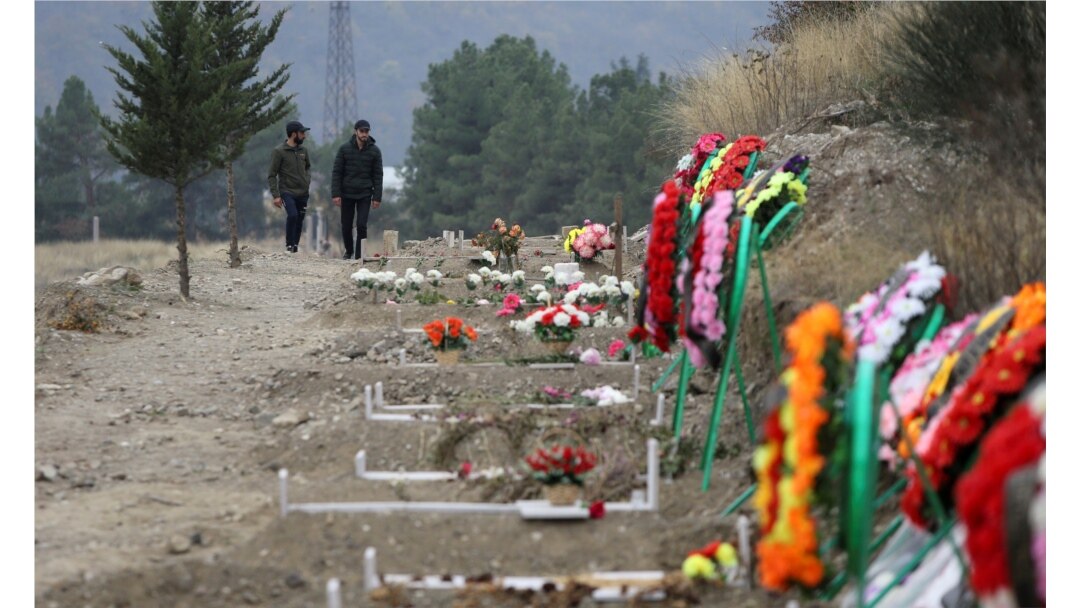 FILE - Men walk along graves of soldiers and civilians who were killed during a military conflict over the breakaway region of Nagorno-Karabakh, in Stepanakert, Nov. 2, 2020.