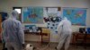 Workers wearing protective suits spray disinfectant inside a classroom at a primary school in Athens, March 9, 2020. 