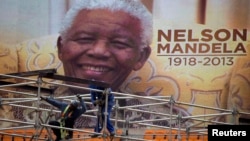 An image of Nelson Mandela is displayed on a digital screen as workers on scaffolding construct a stage ahead of Mandela's national memorial service at First National Bank (FNB) Stadium, also known as Soccer City, in Johannesburg, Dec. 9, 2013.