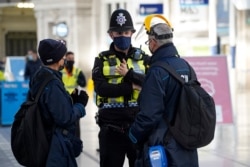 A member of the British Transport Police speaks with travelers at Waterloo Station in London, Dec. 20, 2020.