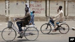 Two boys ride their bicycles past a sign reading "Stop killing Muslims Army" on a wall in Kano, Nigeria, April 8, 2016. Nigeria's Kaduna state government has secretly buried hundreds of minority Shi'ite Muslims in a mass grave.