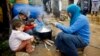 FILE - A Syrian refugee woman with her children prepares food near her tent in a camp for Syrians who fled their country’s civil war, in the Chouf mountain town of Ketermaya, Lebanon. 