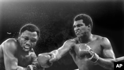 FILE - Spray flies from the head of challenger Joe Frazier as heavyweight champion Muhammad Ali connects with a right in the ninth round of their title fight in Manila, Philippines, Oct. 1, 1974.