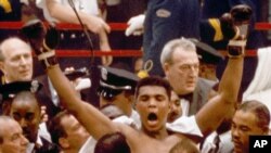 Muhammad Ali, or Cassius Clay at the time, strikes a familiar pose as he shouts "I am the greatest," as he leaves the ring, arms raised, following his defeat of former heavyweight boxing champion Sonny Liston in Miami Beach, Fla., February 25, 1964.