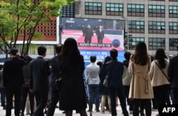 People watch live footage of South Korean President Moon Jae-in (R) walking with North Korean leader Kim Jong Un (L) at the Demilitarized Zone, on a screen in Seoul on April 27, 2018.