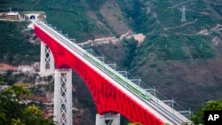 In this photo released by Xinhua News Agency, an electric multiple unit (EMU) train of the China-Laos Railway crosses a major bridge over the Yuanjiang River in southwestern China's Yunnan Province, Dec. 3, 2021. 