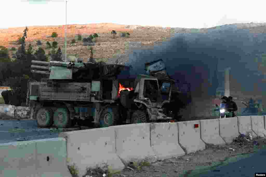People ride a bike next to a burning military vehicle after Syrian rebels announced that they have ousted Syria's Bashar al-Assad, in Damascus.