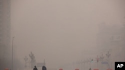 2012年1月18日两名行人走过被雾霾笼罩的北京街头