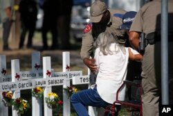 Polisi membantu seorang perempuan setelah dia memberi hormat di depan salib dengan nama anak-anak yang terbunuh di luar Sekolah Dasar Robb di Uvalde, Texas Kamis, 26 Mei 2022. (Foto: AP)