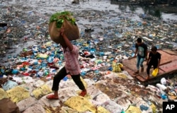 Seorang pria sedang memanggul sekarung sayuran berjalan melewati kanal yang dicemari sampah kantong plastik dan sampah lainnya di Mumbai, India. (Foto:dok)