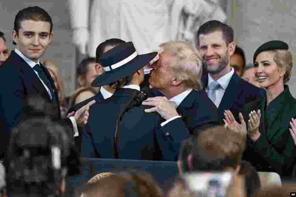 O Presidente Donald Trump, ao centro, à direita, estica-se para beijar a sua mulher Melania Trump enquanto os seus filhos assistem durante a 60ª tomada de posse Presidencial na Rotunda do Capitólio dos EUA, em Washington, a 20 de janeiro de 2025.
