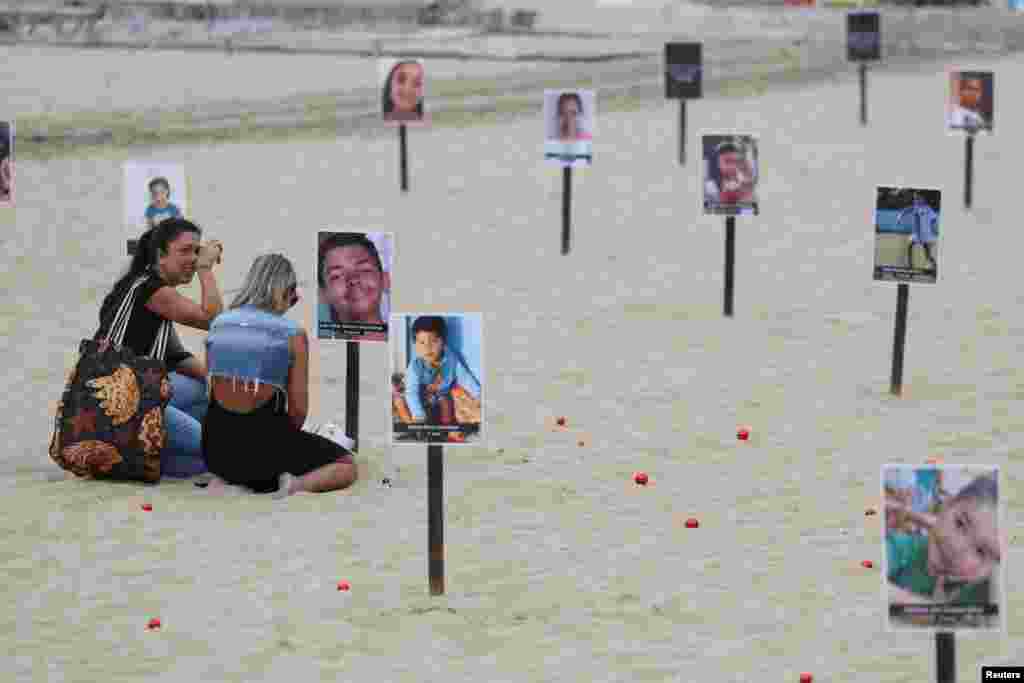 Vanessa Freitas Moreira sits next to the photo of her son Joao Vitor Moreira dos Santos, in a demonstration of NGO Rio de Paz displaying pictures of children who were shot dead during police operations during the administration of Rio de Janeiro's governor Claudio Castro, at Copacabana beach in Rio de Janeiro, Brazil.