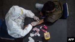 Seorang petugas kesehatan (kiri) mengambil sampel darah dari seorang pengendara motor yang melanggar Pembatasan Sosial Berskala Besar (PSBB) di sebuah kantor polisi di Surabaya, 3 Mei 2020. (Foto: AFP)