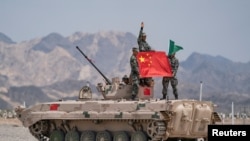 Tentara China dari Tentara Pembebasan Rakyat (PLA) berpose untuk foto dengan bendera nasional China di sebuah tank di Korla, Daerah Otonomi Uighur Xinjiang. (Foto: Reuters)