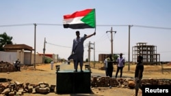 FILE - A Sudanese protester holds a national flag as he stands on a barricade along a street, in Khartoum, Sudan, June 5, 2019.