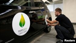 FILE - An employee installs a sticker which reads 100% electric next to the logo of the upcoming COP21 Climate Change Conference on a Nissan LEAF electric car in Boulogne-Billancourt, near Paris, France.