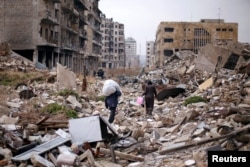 FILE - People walk amid the rubble as they carry belongings that they collected from their houses in the government controlled area of Aleppo, Syria, Dec. 17, 2016.