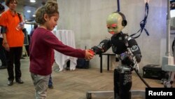 Seorang anak perempuan memberikan bola kepada sebuah robot dalam sebuah Pameran Robot Manusia di Madrid, 19/11/2014.
