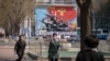FILE - People wearing face masks walk before a propaganda poster displayed on a street in Pyongyang, April 9, 2020. 