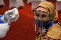 Seorang perempuan yang memakai masker dan pelindung wajah terlihat saat petugas kesehatan bersiap untuk menyuntiknya dengan vaksin Sinovac selama program vaksinasi massal COVID-19 di Bursa Efek Indonesia di Jakarta, 31 Maret 2021. (Foto: REUTERS/Willy Kurniawa)
