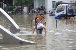 河南省鄭州市一名男子背著一名女子趟過滿是洪水的街道。 （2021年7月21日）