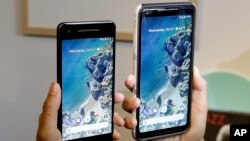 FILE - A woman holds up the Google Pixel 2 phone, left, next to the Pixel 2 XL phone at a Google event at the SFJAZZ Center in San Francisco, Oct. 4, 2017.