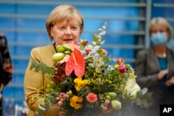 Kanselir Jerman Angela Merkel memegang karangan bunga dari Wakil Rektor dan Menteri Keuangan Olaf, Scholz sebelum rapat kabinet di kanselir di Berlin, 24 November 2021. (Foto: AP)