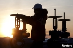 FILE - A worker checks the valve of an oil pipe at the Lukoil company owned Imilorskoye oil field outside the Siberian city of Kogalym, Russia, Jan. 25, 2016.