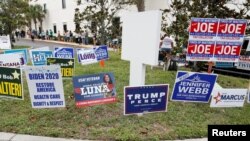 FILE - Campaign signs are posted near the Supervisor of Elections Office polling station while people line up for early voting in Pinellas County ahead of the election in Largo, Florida., Oct. 21, 2020.
