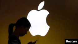 Seorang perempuan memperhatikan layar ponselnya di depan logo Apple di luar toko Apple di Shanghai. (Foto:dok)