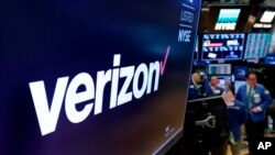 FILE- This April 23, 2018, file photo shows the logo for Verizon above a trading post on the floor of the New York Stock Exchange. Cellular companies such as Verizon are looking to challenge traditional cable companies with residential internet service that promises to be ultra-fast, affordable and wireless. Using an emerging wireless technology known as 5G, Verizon’s 5G Home service provides an alternative to cable for connecting laptops, phones, TVs and other devices over Wi-Fi. It launches in four U.S. cities on Monday, Oct. 1.