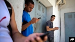 FILE - Students gather behind a business looking for a Internet signal for their smart phones in Havana, Cuba, April 1, 2014.